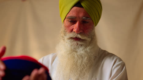 Fotografía-De-Estudio-De-Un-Hombre-Sikh-Mayor-Que-Ayuda-A-Un-Hombre-Sikh-Más-Joven-A-Atar-La-Tela-Para-Un-Turbante-Contra-Un-Fondo-Liso,-Filmada-En-Tiempo-Real-5